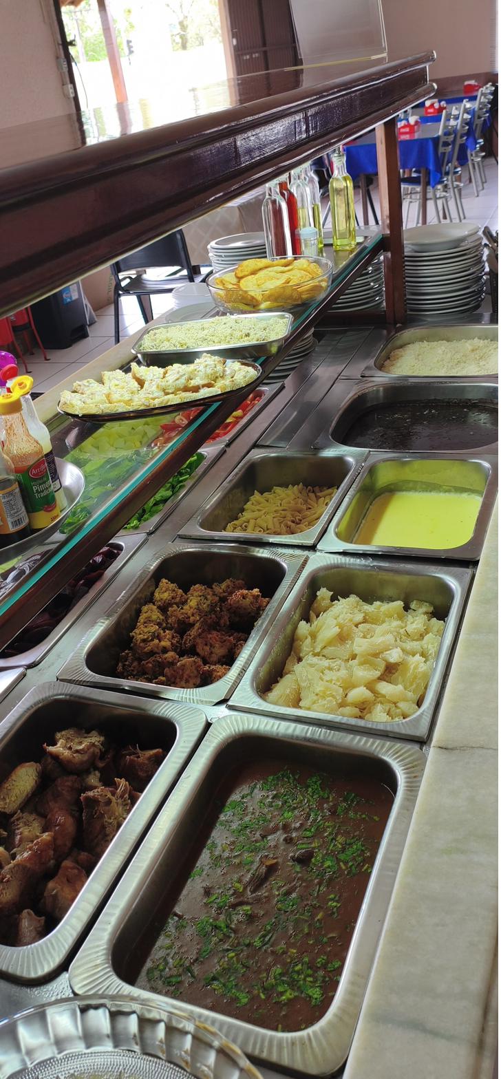 Pratos quentes do buffet: macarrão, mandioca cozida, bolinhos fritos, carnes e feijão com cheiro-verde