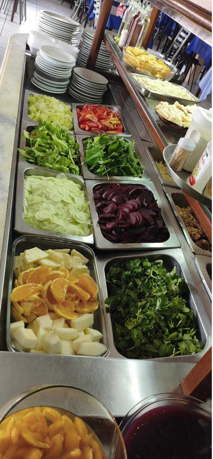 Balcão de saladas do buffet com alface, rúcula, agrião, pepino, beterraba, tomate, laranja e abacaxi