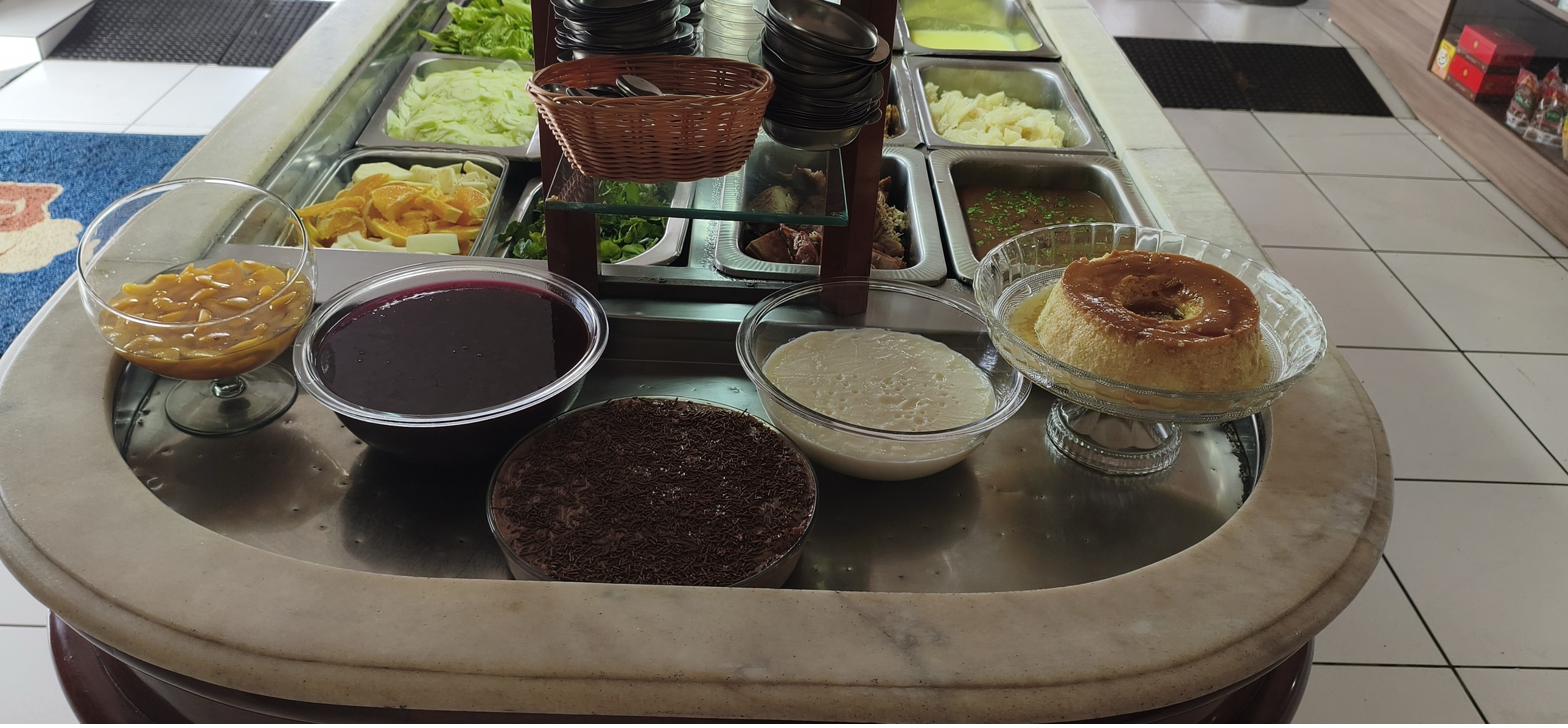 Mesa de sobremesas com pêssego em calda, gelatina, mousse de chocolate com granulado, creme branco e pudim